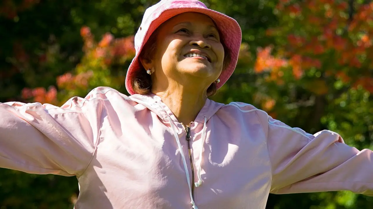 A smiling senior woman with her arms open outdoors